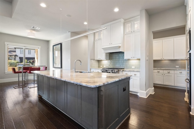 kitchen featuring light stone counters, an island with sink, decorative backsplash, and white cabinets