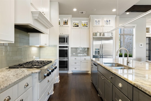 kitchen featuring sink, built in appliances, light stone counters, white cabinets, and decorative backsplash