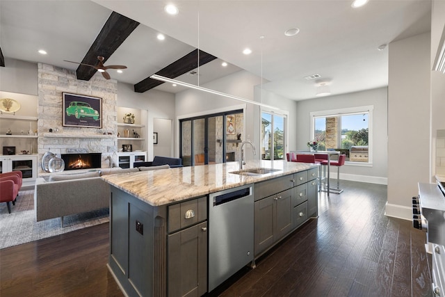 kitchen featuring sink, a kitchen island with sink, light stone counters, a stone fireplace, and stainless steel dishwasher