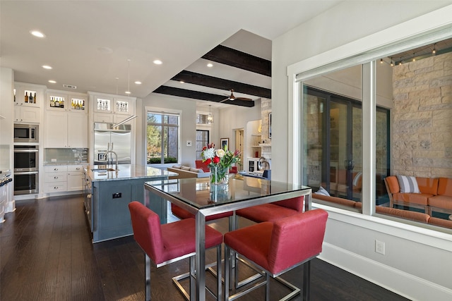 kitchen with tasteful backsplash, built in appliances, an island with sink, beam ceiling, and white cabinets