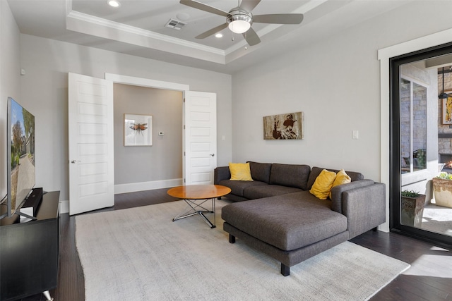 living room featuring dark hardwood / wood-style flooring, a tray ceiling, ornamental molding, and ceiling fan