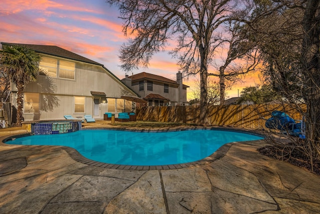 pool at dusk featuring a patio and an in ground hot tub