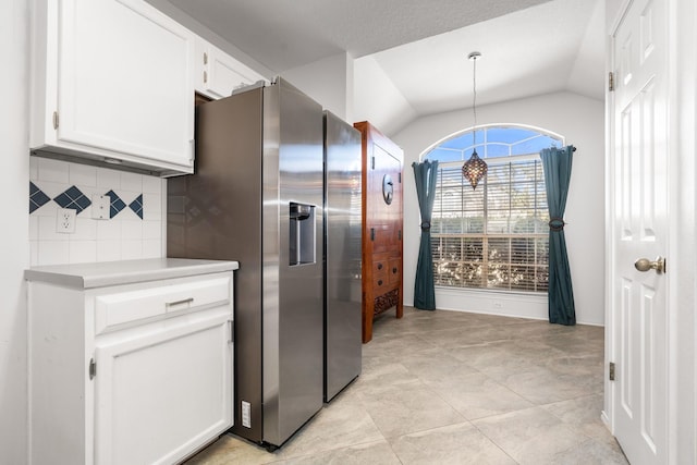 kitchen featuring pendant lighting, lofted ceiling, white cabinetry, stainless steel refrigerator with ice dispenser, and tasteful backsplash