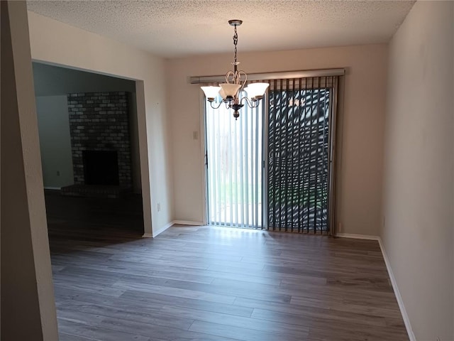 unfurnished dining area featuring dark wood-type flooring, a brick fireplace, a chandelier, and a textured ceiling