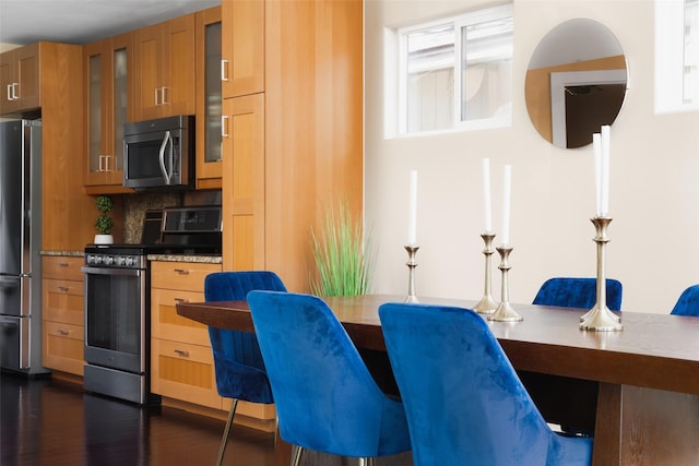 kitchen with tasteful backsplash, light stone counters, dark wood-type flooring, and appliances with stainless steel finishes