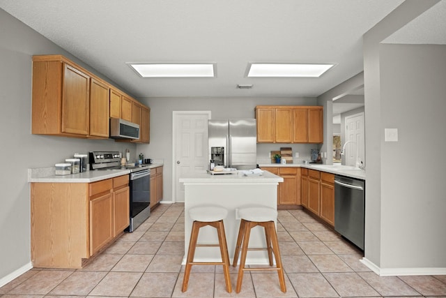 kitchen with appliances with stainless steel finishes, a center island, sink, and light tile patterned floors