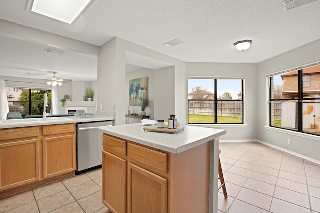 kitchen with sink, a textured ceiling, light tile patterned floors, stainless steel dishwasher, and a kitchen island