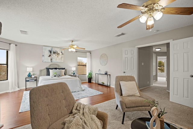 bedroom featuring multiple windows, hardwood / wood-style floors, a textured ceiling, and ceiling fan