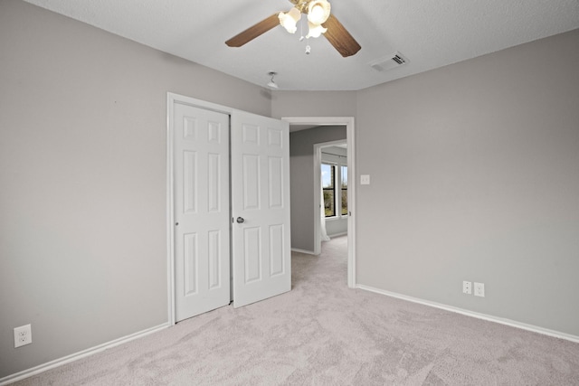 unfurnished bedroom featuring light carpet, a textured ceiling, a closet, and ceiling fan