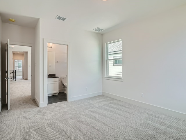 unfurnished bedroom featuring multiple windows, ensuite bath, and light colored carpet