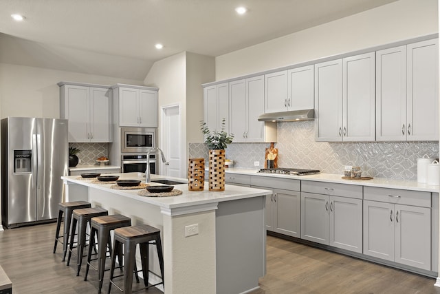 kitchen featuring gray cabinets, an island with sink, appliances with stainless steel finishes, and a kitchen bar