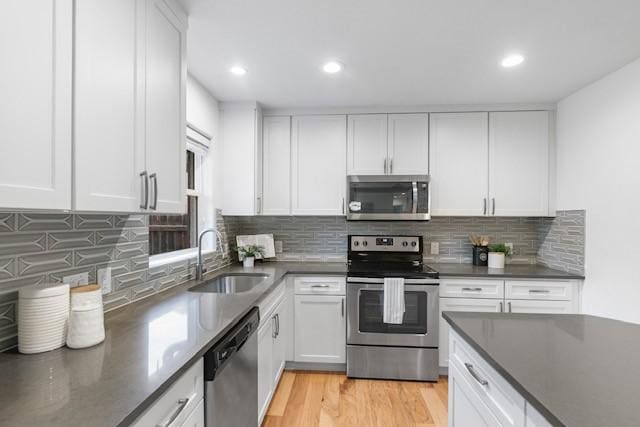 kitchen featuring sink, white cabinetry, light hardwood / wood-style flooring, stainless steel appliances, and decorative backsplash