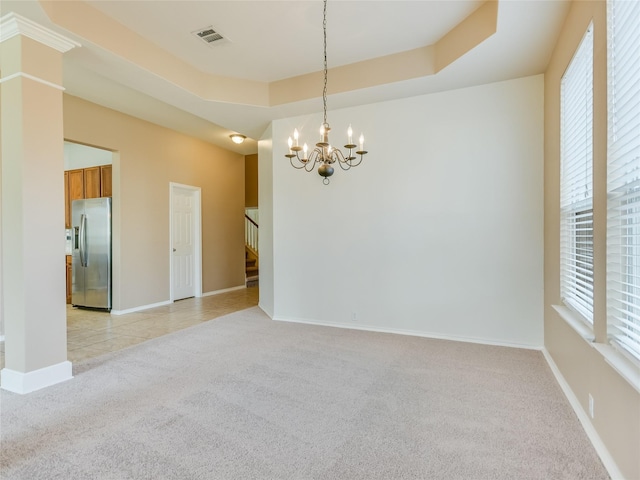 empty room featuring an inviting chandelier, a tray ceiling, and light colored carpet