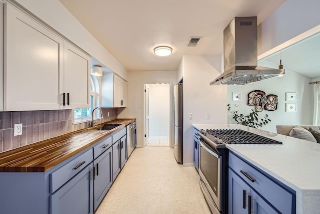 kitchen featuring appliances with stainless steel finishes, island range hood, sink, white cabinets, and blue cabinetry