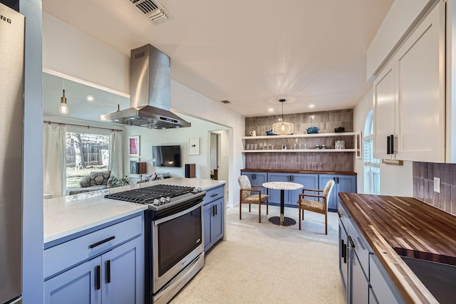 kitchen with island range hood, butcher block counters, white cabinets, hanging light fixtures, and stainless steel gas range