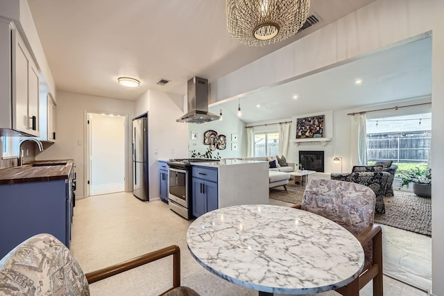 kitchen featuring appliances with stainless steel finishes, island range hood, white cabinetry, sink, and butcher block counters