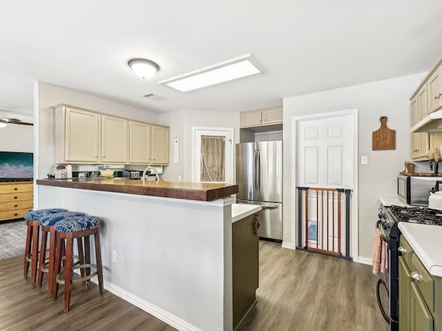 kitchen with a breakfast bar, butcher block counters, hardwood / wood-style floors, stainless steel appliances, and cream cabinetry