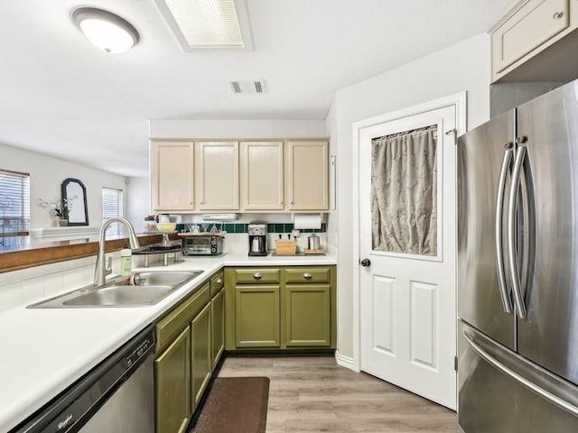 kitchen with stainless steel appliances, sink, green cabinets, and light wood-type flooring