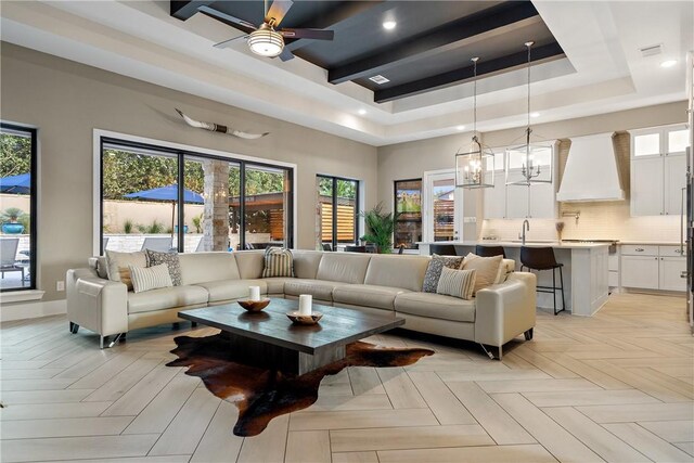 living room featuring sink, a tray ceiling, ceiling fan with notable chandelier, and light parquet floors