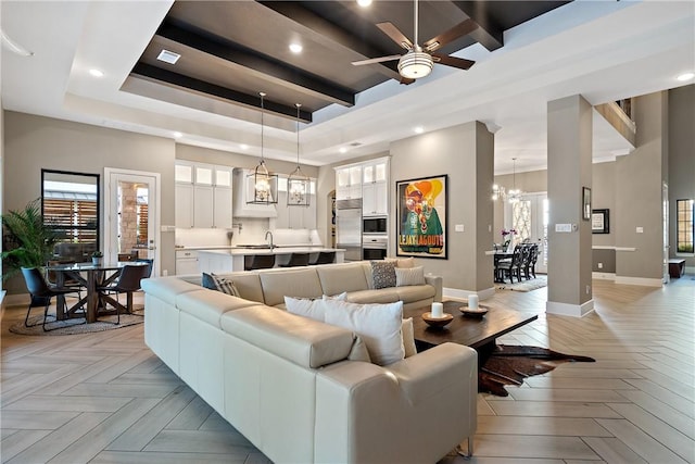 living room featuring light parquet flooring, sink, ceiling fan with notable chandelier, and a tray ceiling