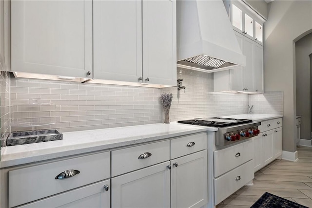 kitchen with premium range hood, stainless steel gas stovetop, backsplash, white cabinets, and light stone counters