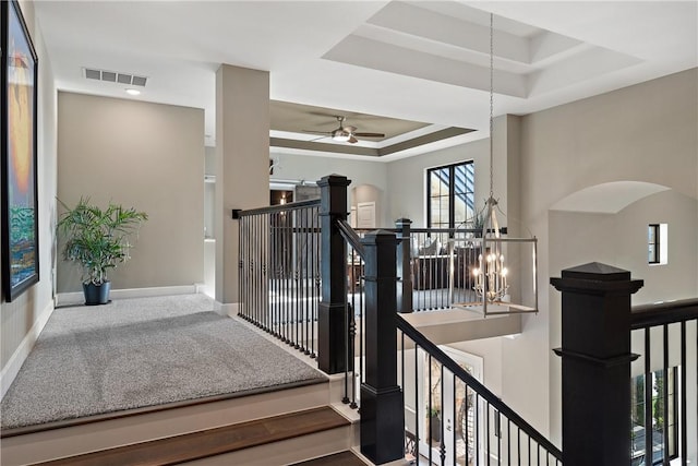 stairway featuring carpet floors, ceiling fan with notable chandelier, and a tray ceiling