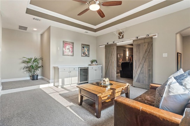 living room with a barn door, light colored carpet, a tray ceiling, and beverage cooler