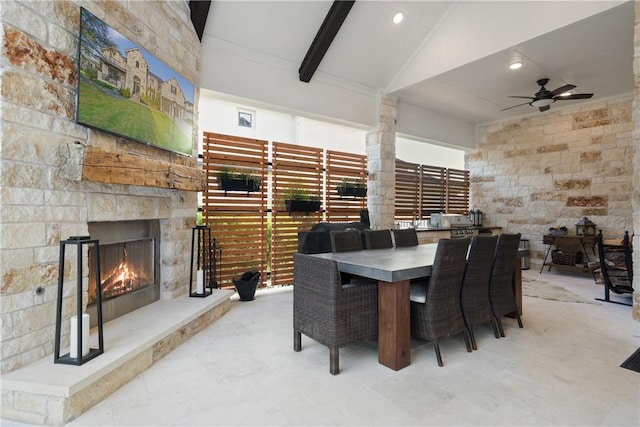 dining area featuring vaulted ceiling with beams, ceiling fan, and an outdoor stone fireplace