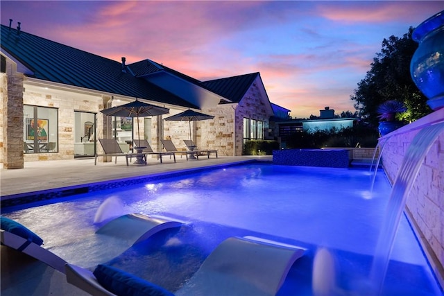 pool at dusk with a patio and pool water feature