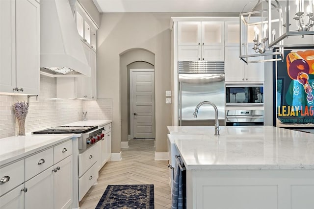 107 Bisset Ct, Austin, TX 78738 - kitchen with built in appliances, custom range hood, backsplash, white cabinets, and light stone counters