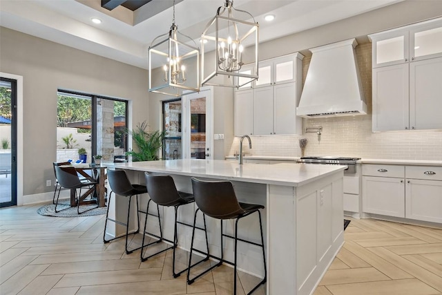 107 Bisset Ct, Austin, TX 78738 - kitchen featuring custom exhaust hood, a center island with sink, light countertops, white cabinetry, and tasteful backsplash