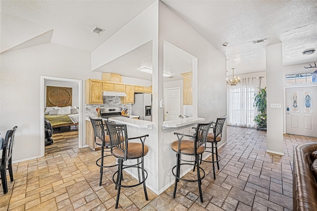 kitchen featuring a breakfast bar area, an inviting chandelier, stainless steel appliances, a textured ceiling, and light brown cabinets