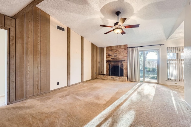 unfurnished living room featuring a fireplace, wood walls, ceiling fan, light carpet, and a textured ceiling