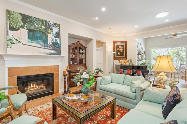 living room featuring a tiled fireplace, light tile patterned flooring, ceiling fan, and crown molding