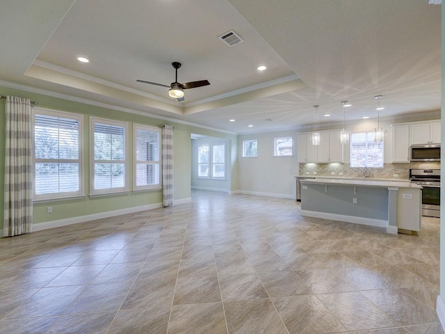 unfurnished living room featuring ceiling fan, ornamental molding, a tray ceiling, and sink