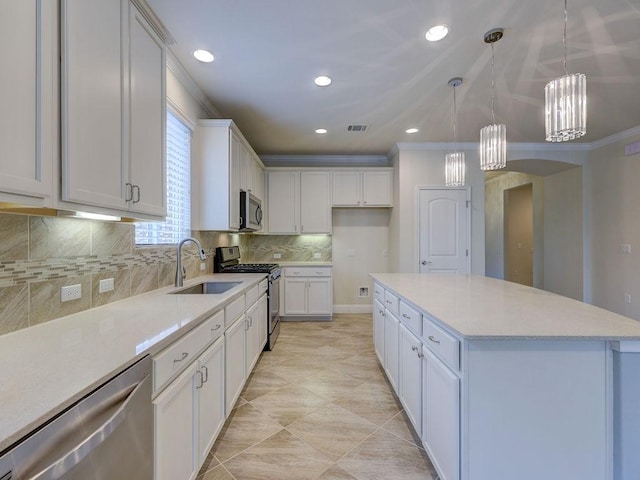 kitchen with white cabinetry, hanging light fixtures, ornamental molding, appliances with stainless steel finishes, and a kitchen island