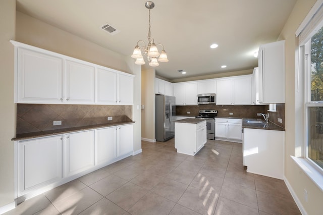 kitchen with light tile patterned flooring, appliances with stainless steel finishes, white cabinetry, sink, and a center island