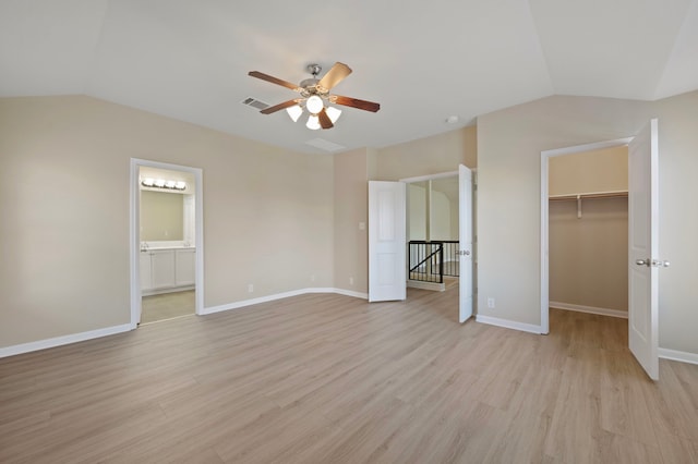 unfurnished bedroom featuring lofted ceiling, a walk in closet, ceiling fan, ensuite bath, and light hardwood / wood-style flooring