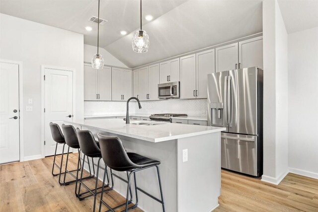 kitchen with sink, appliances with stainless steel finishes, a kitchen island with sink, backsplash, and decorative light fixtures