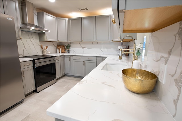 kitchen with light stone countertops, appliances with stainless steel finishes, gray cabinetry, and wall chimney range hood