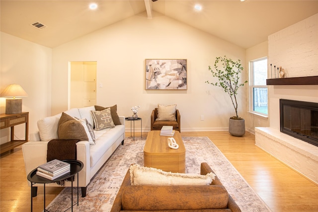 living room featuring a stone fireplace, lofted ceiling with beams, and light hardwood / wood-style flooring