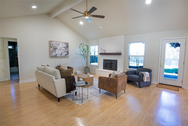 living room with beam ceiling, a fireplace, light hardwood / wood-style floors, and ceiling fan