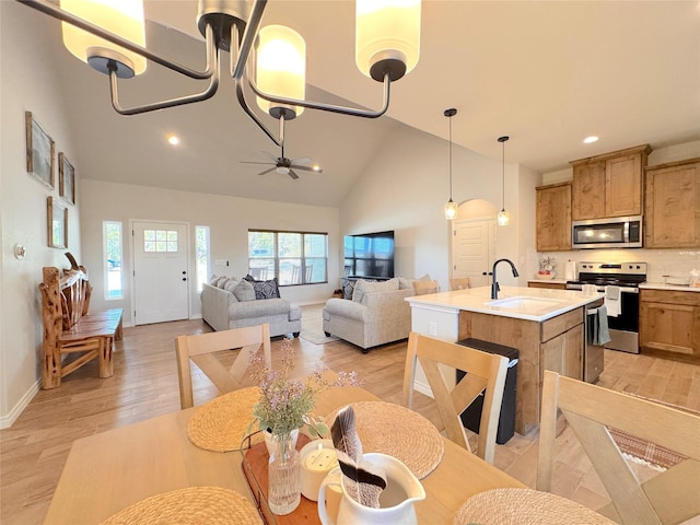 kitchen with sink, decorative light fixtures, appliances with stainless steel finishes, an island with sink, and light hardwood / wood-style floors