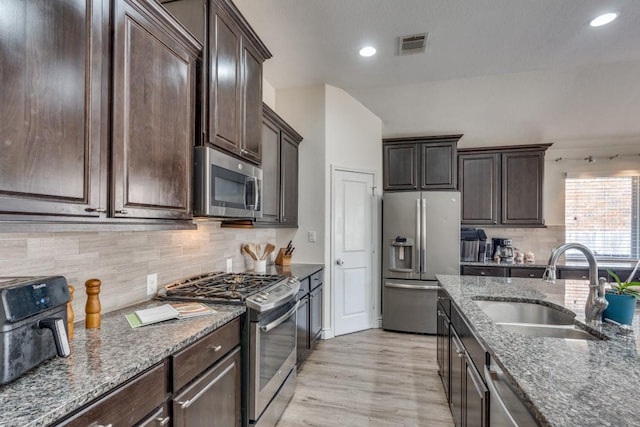 kitchen with sink, dark brown cabinets, dark stone counters, stainless steel appliances, and decorative backsplash