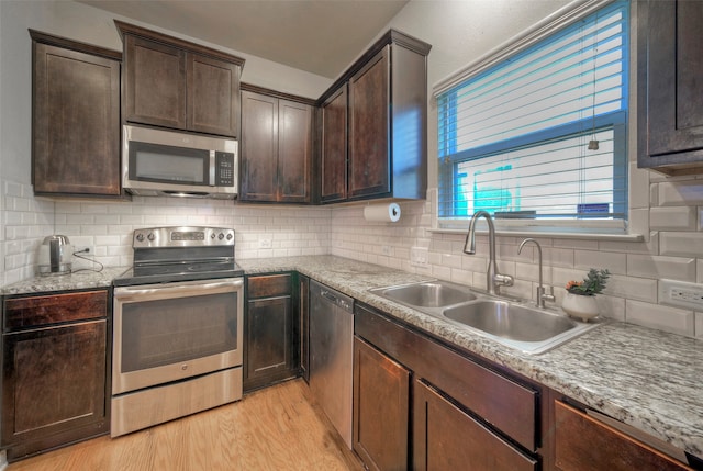 kitchen featuring stainless steel appliances, dark brown cabinets, sink, and light wood-type flooring