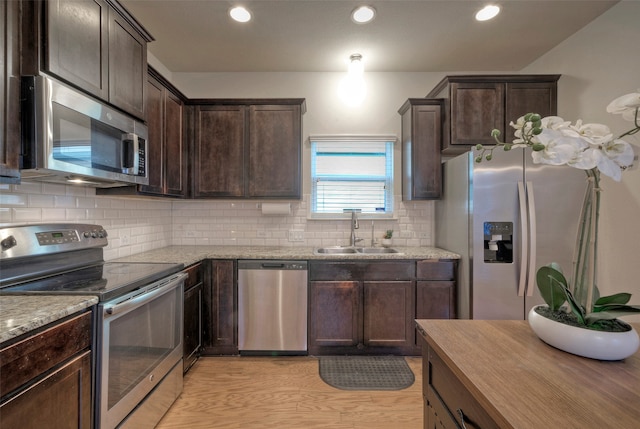 kitchen featuring light stone countertops, appliances with stainless steel finishes, sink, and light wood-type flooring