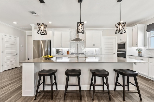 kitchen featuring stainless steel appliances, decorative light fixtures, and an island with sink