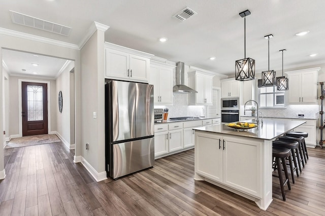 kitchen featuring wall chimney range hood, a breakfast bar area, a kitchen island with sink, hanging light fixtures, and stainless steel appliances