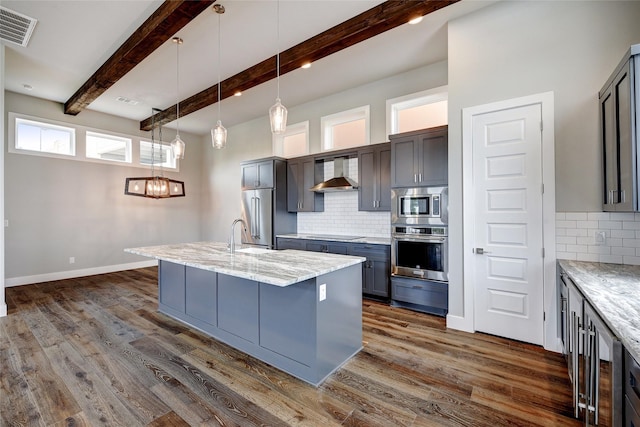 kitchen with appliances with stainless steel finishes, a kitchen island with sink, wall chimney range hood, and backsplash