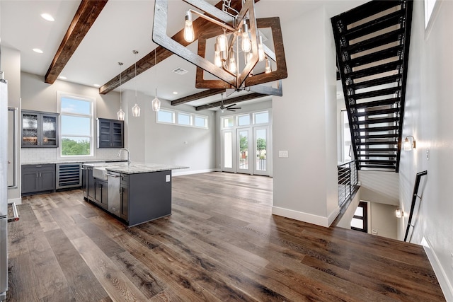 kitchen with beam ceiling, tasteful backsplash, an island with sink, pendant lighting, and beverage cooler